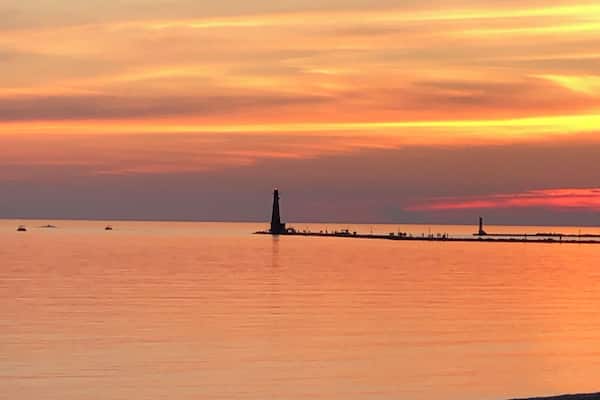 Ein Sonnenuntergang über einem ruhigen Meer mit einem Leuchtturm und einer anlegenden Mole.
