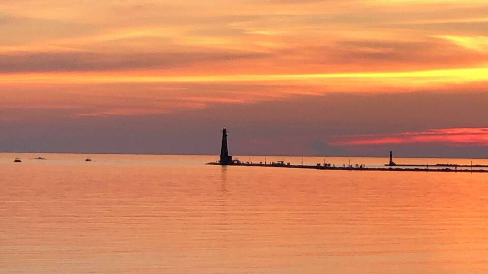 A sunset over a calm sea with a lighthouse and a pier extending into the water.