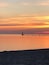 A sunset over a calm sea with a lighthouse and a pier extending into the water.