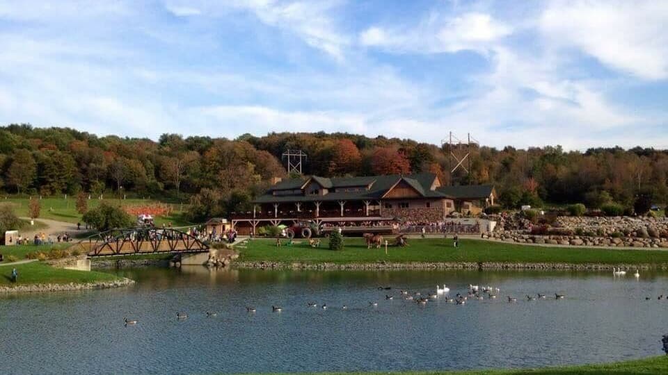 A lakeside view with a bridge, a building with a green roof, and a forested hill in the background.
