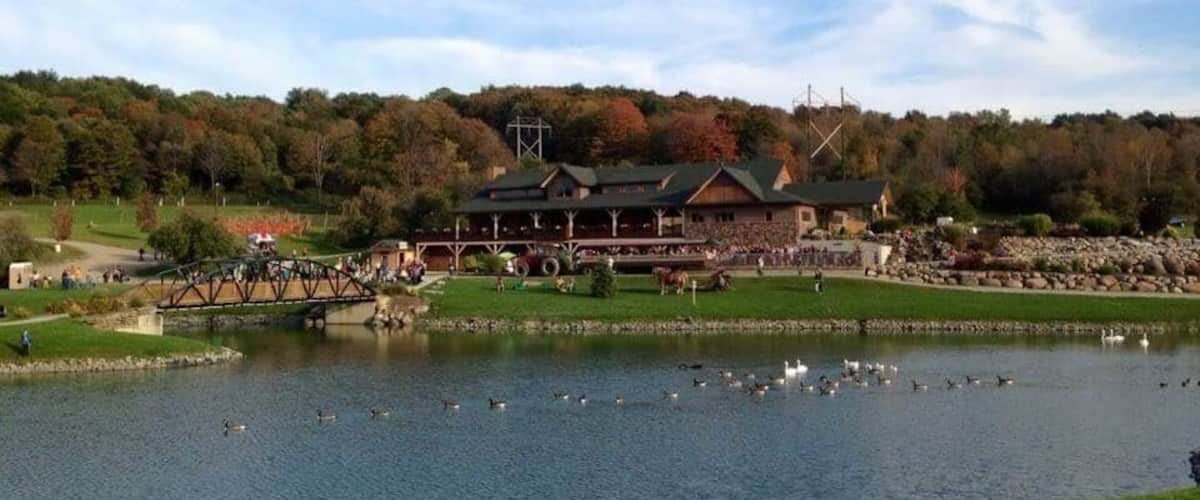 A lakeside view with a bridge, a building with a green roof, and a forested hill in the background.