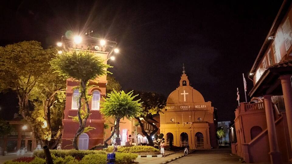 Una iglesia con cúpula y cruz, rodeada de árboles e iluminada por farolas.