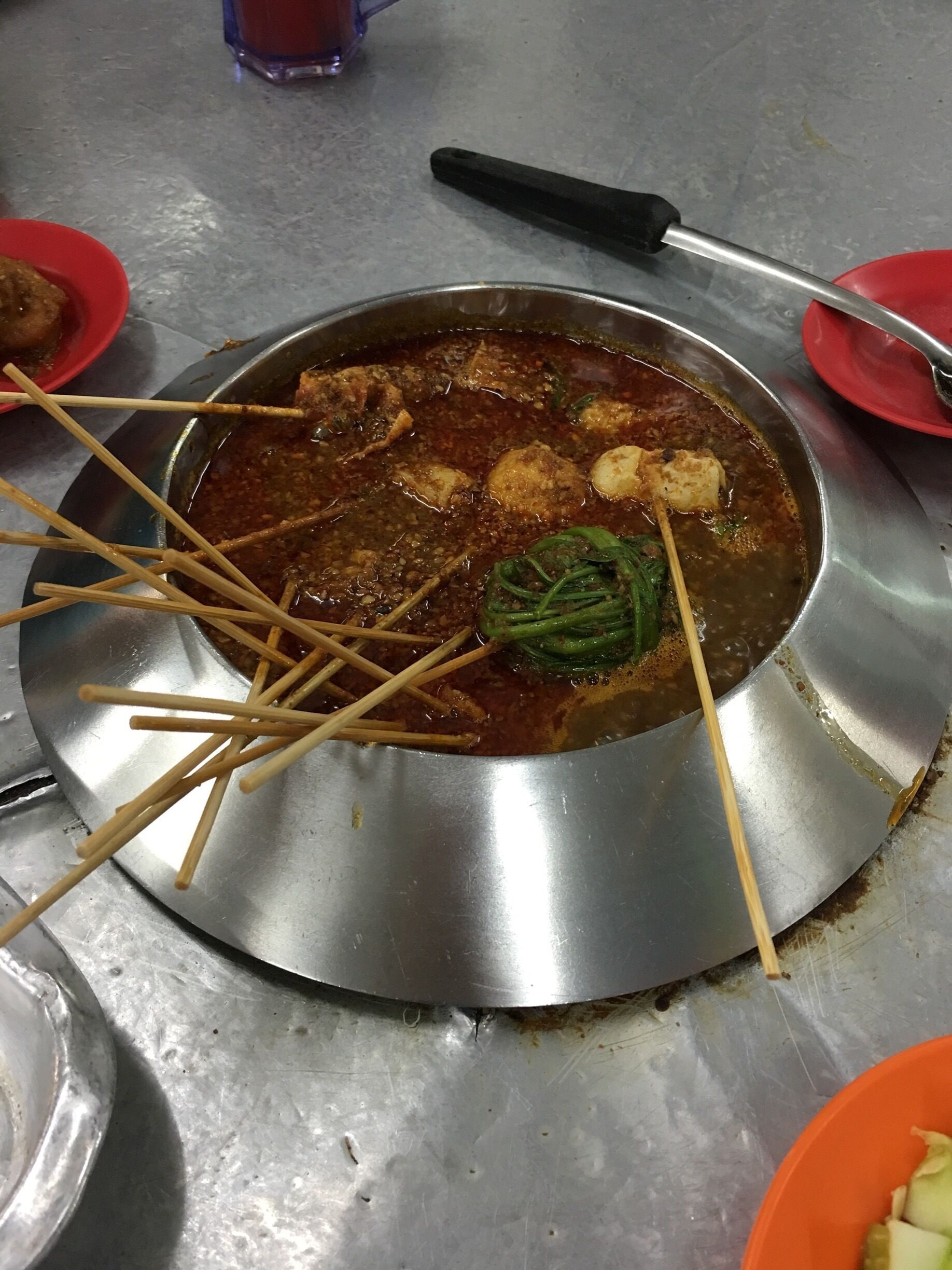 A metal pot with a stew containing meat and vegetables, surrounded by skewers and a knife.