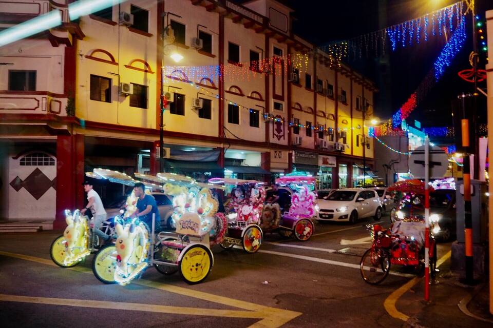 A street at night with brightly lit decorations and a building with a sign that reads "JAC".