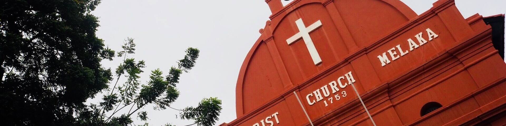A red church with a cross and the name "CHRIST" and "NELAKA" on its facade.