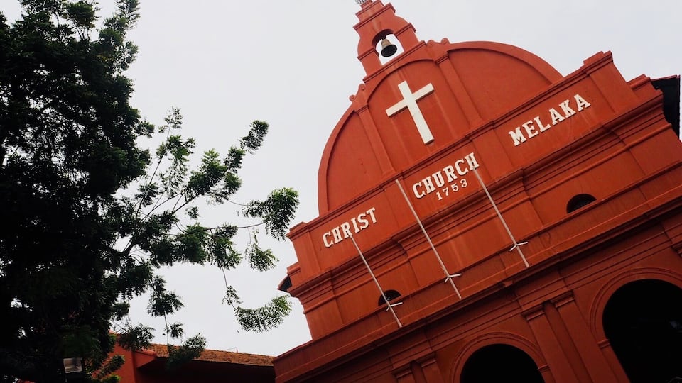 A red church with a cross and the name "CHRIST" and "NELAKA" on its facade.
