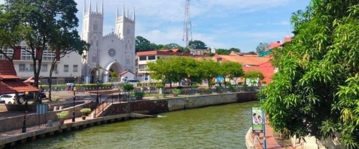 A river with a bridge, a church with two towers, and a red-roofed building.