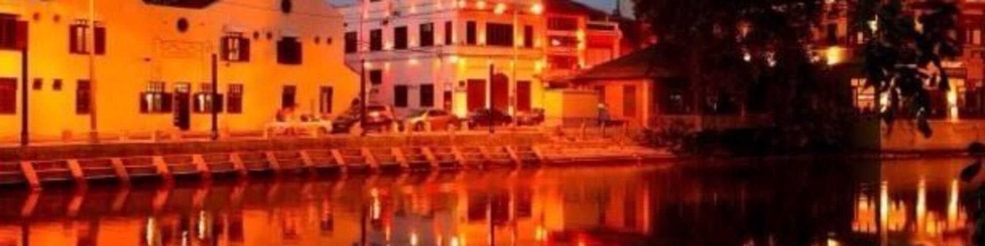 A waterfront with illuminated buildings reflecting on the water at dusk.
