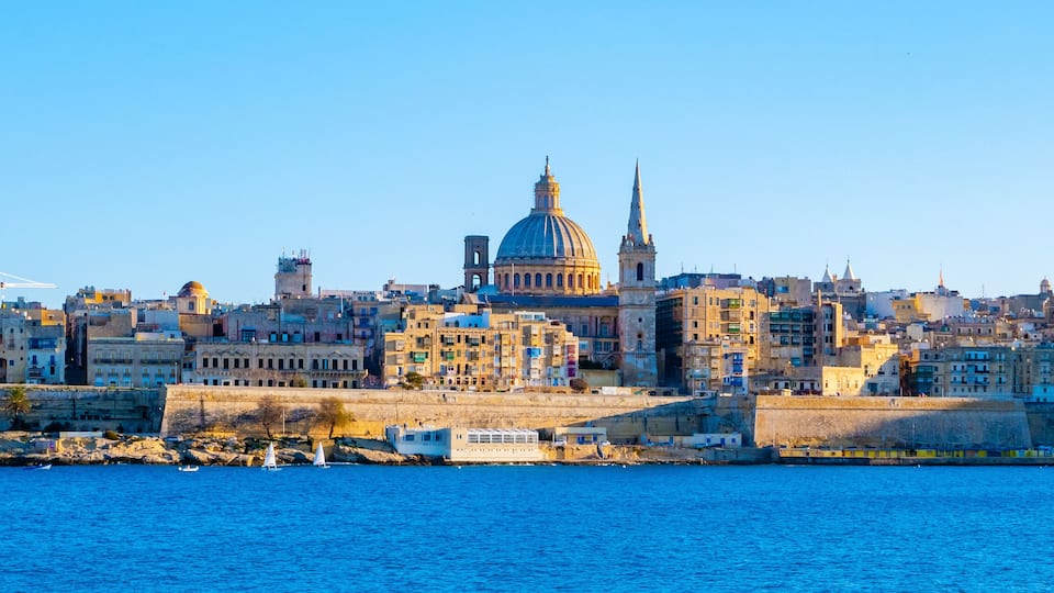 A coastal cityscape with a prominent domed cathedral and a tall spire.