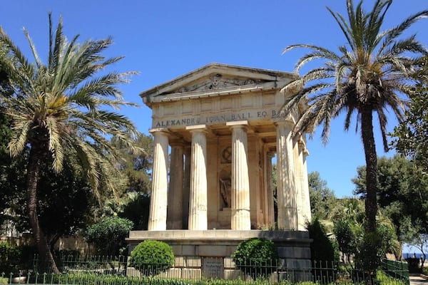 Ein klassischer griechischer Tempel mit Säulen, umgeben von Palmen und blauem Himmel.