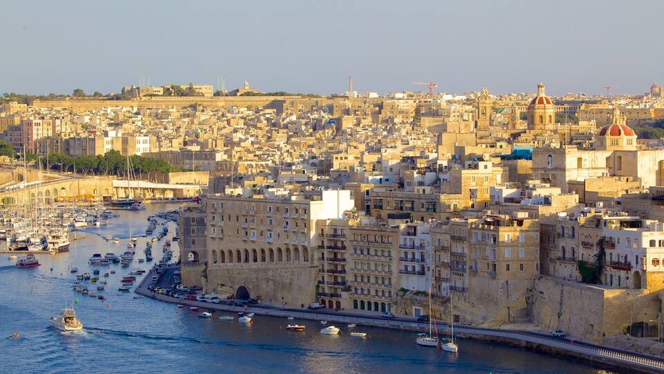 A densely packed cityscape with historic architecture, a harbor filled with boats, and a prominent fortress-like building.