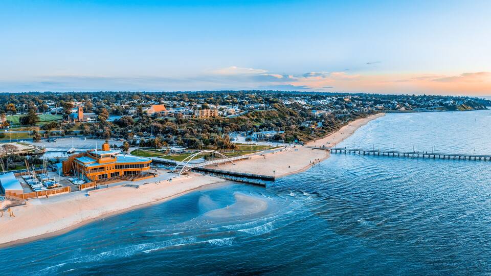An aerial view of a coastal town with a beach, a pier, and a prominent orange building.