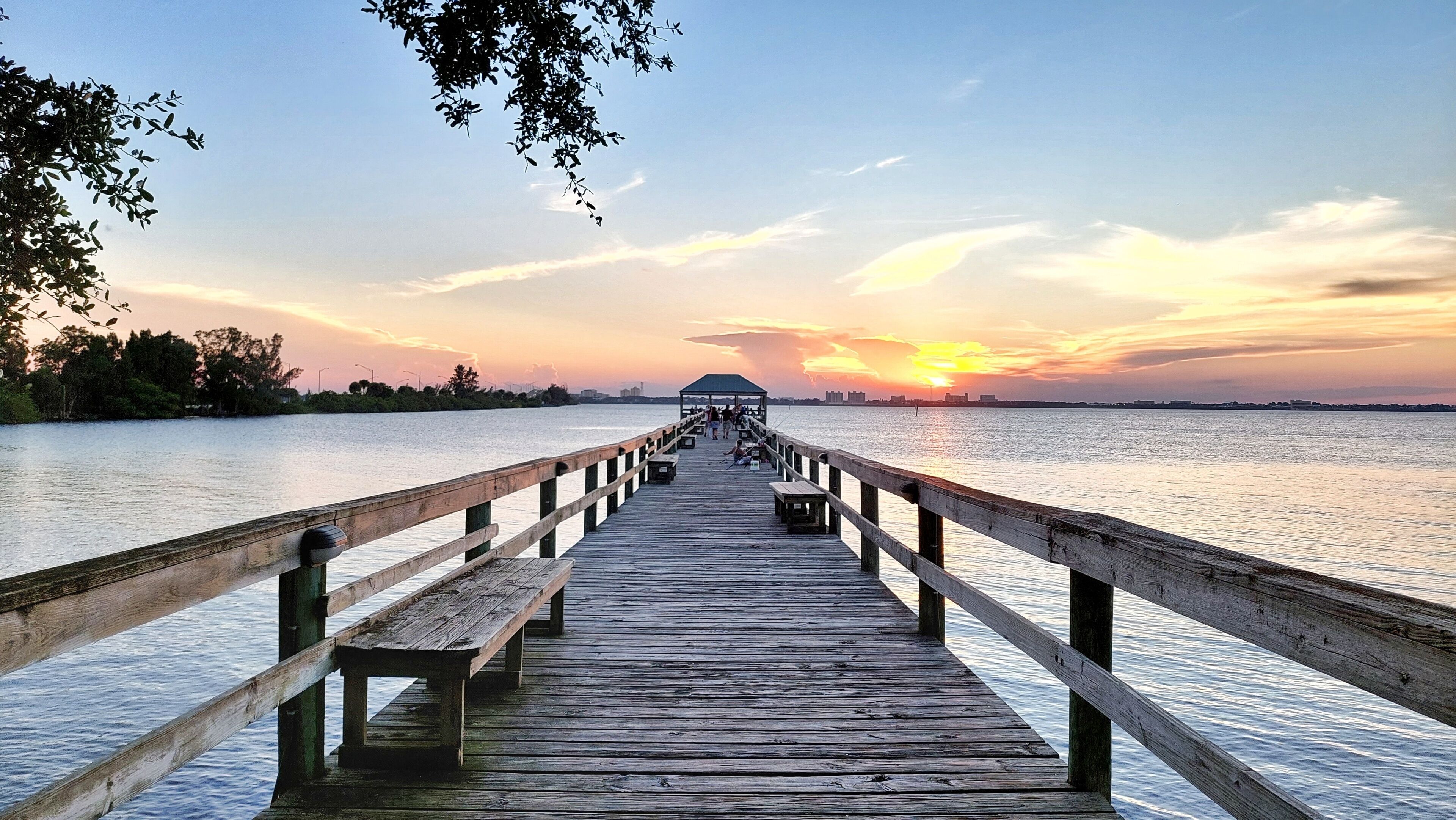 A wooden pier extending into calm water with a sunset in the background.