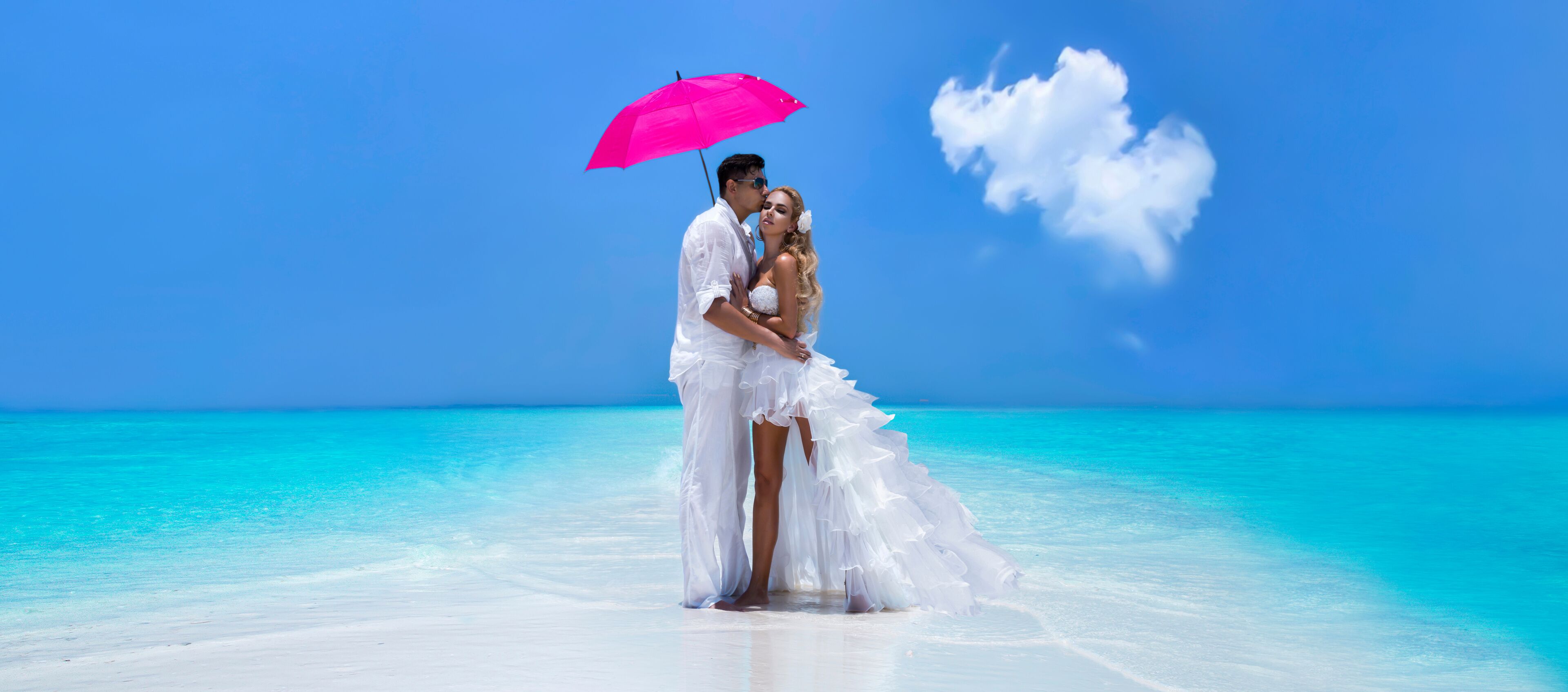 Summer love. Beautiful happy young couple in wedding clothes and pink umbrella is standing on a beach in the Maldives. Engagements and wedding on the beach on the paradise island of Maldives.