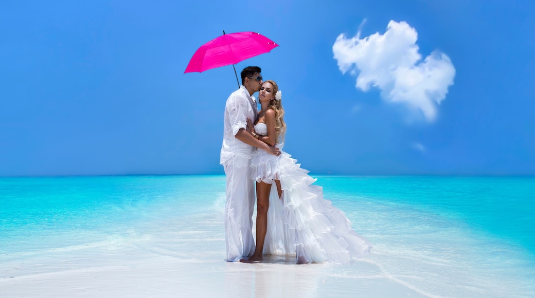 Summer love. Beautiful happy young couple in wedding clothes and pink umbrella is standing on a beach in the Maldives. Engagements and wedding on the beach on the paradise island of Maldives.