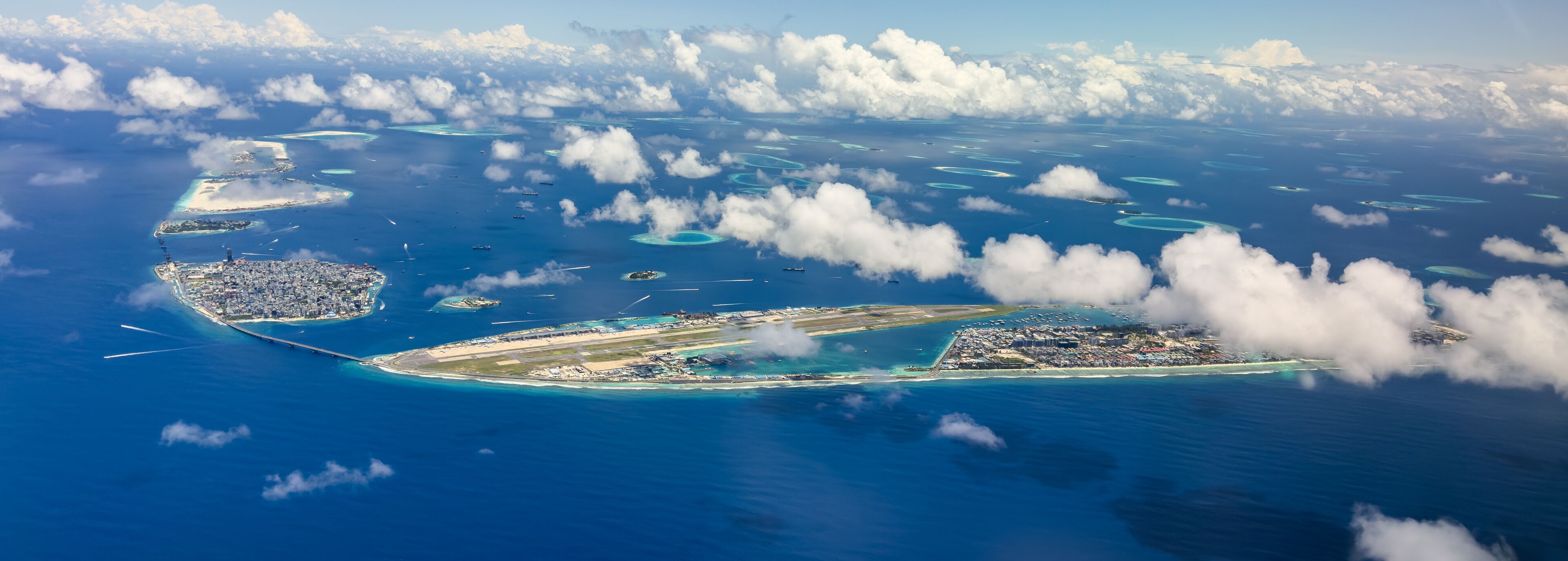 An aerial view of a tropical island with clear blue waters, numerous small islands, and a large airport.
