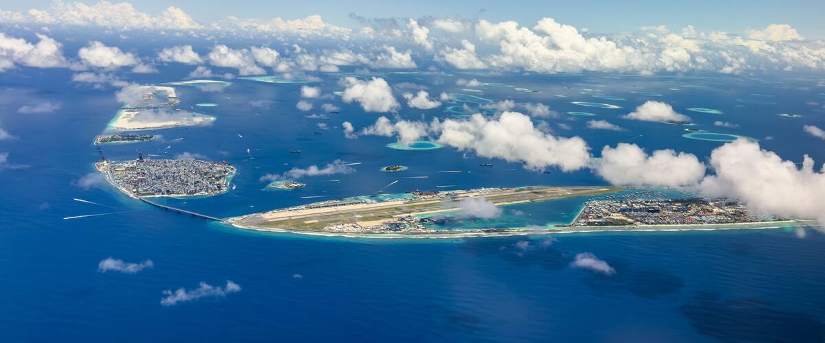 An aerial view of a tropical island with clear blue waters, numerous small islands, and a large airport.