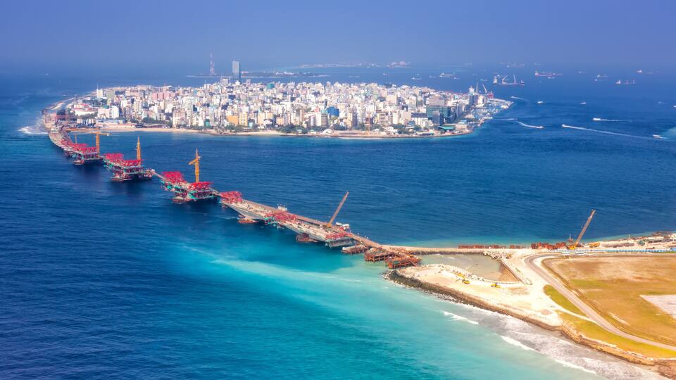 An aerial view of a coastal city with a prominent port area featuring several large cranes and ships.