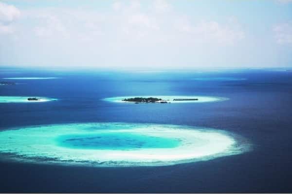 Un lagon turquoise bordé d’une barrière de corail, avec de petites îles qui se dessinent à l’horizon.