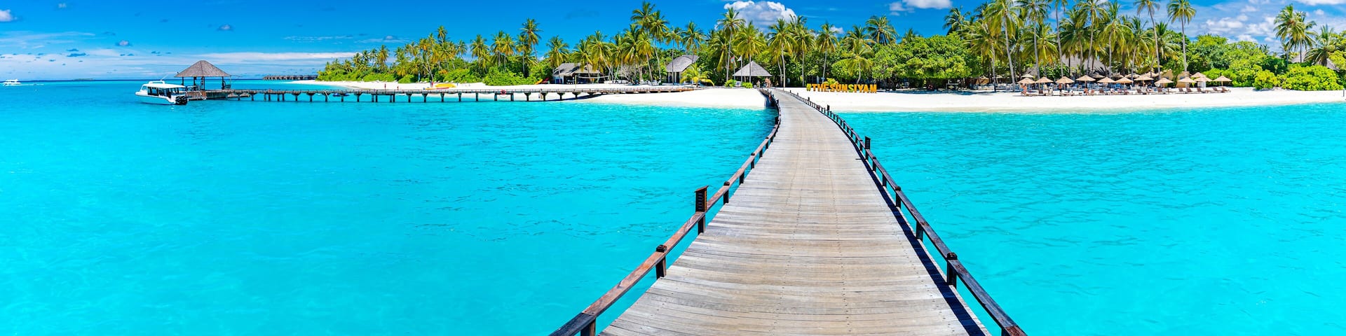 Maldives island beach panorama. Palm trees and beach bar and long wooden pier pathway. Tropical vacation and summer holiday background concept