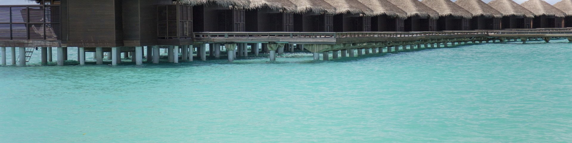 Overwater bungalows with thatched roofs on stilts over turquoise water.