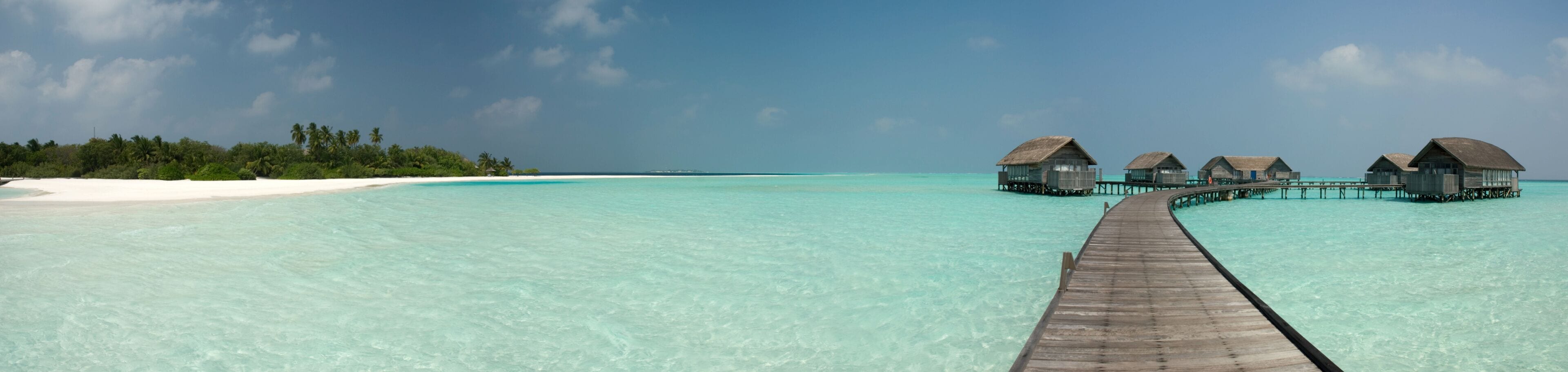 A wooden pier leading to overwater bungalows in clear turquoise waters.