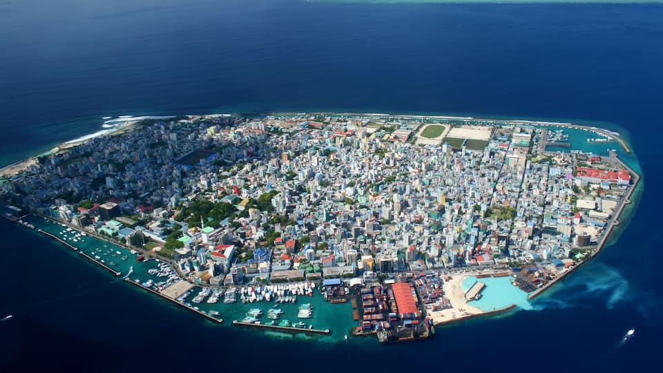 An aerial view of a densely populated island with a marina, buildings, and clear blue waters.