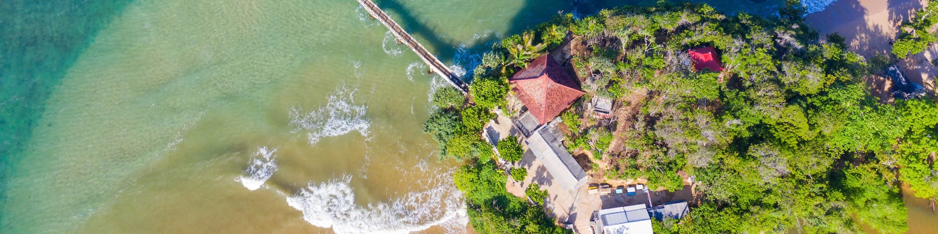 An aerial view of a coastal area with a beach, a pier, and a small island with buildings.