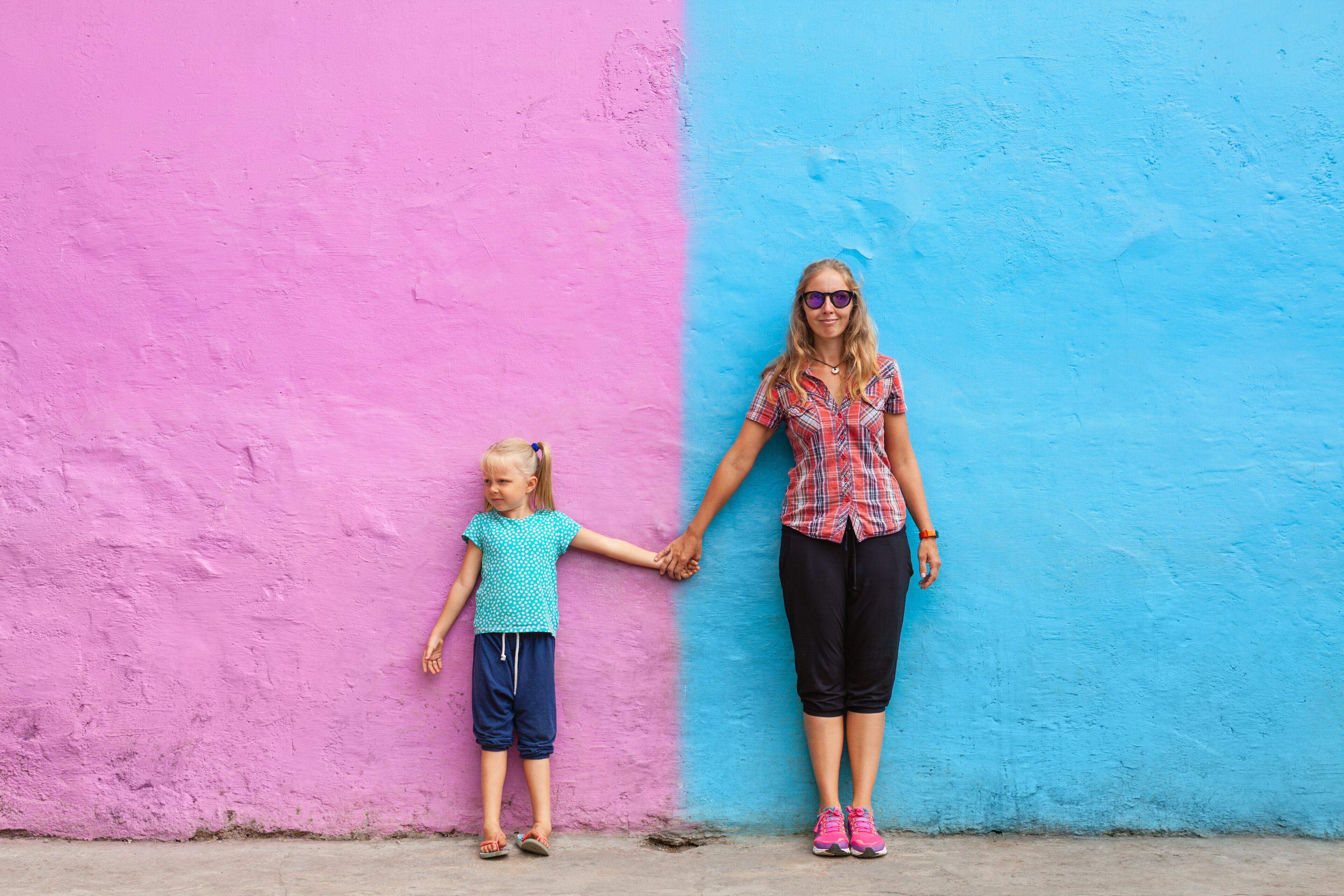 Mother, daughter standing hand in hand against bright pink and blue wall in Kampung Warna Warni Jodipan. Fun and colorful travel. Family bonding, local culture and urban street art in Southeast Asia