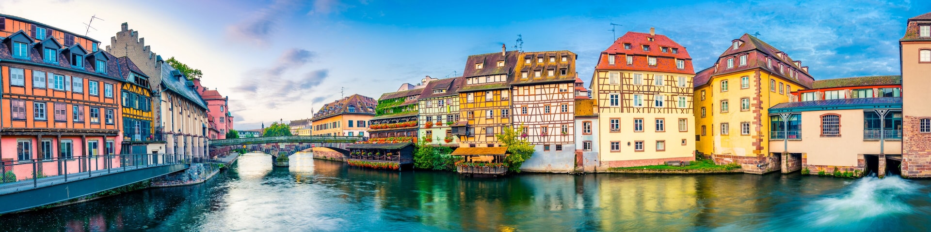 A river with a bridge, colorful half-timbered buildings, and a clear blue sky.