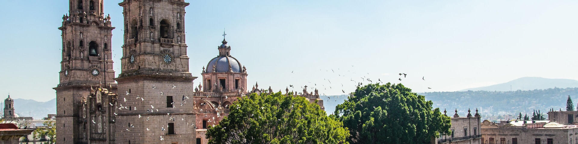 A historic cathedral with two prominent towers and a large dome, surrounded by a well-maintained square with trimmed hedges.