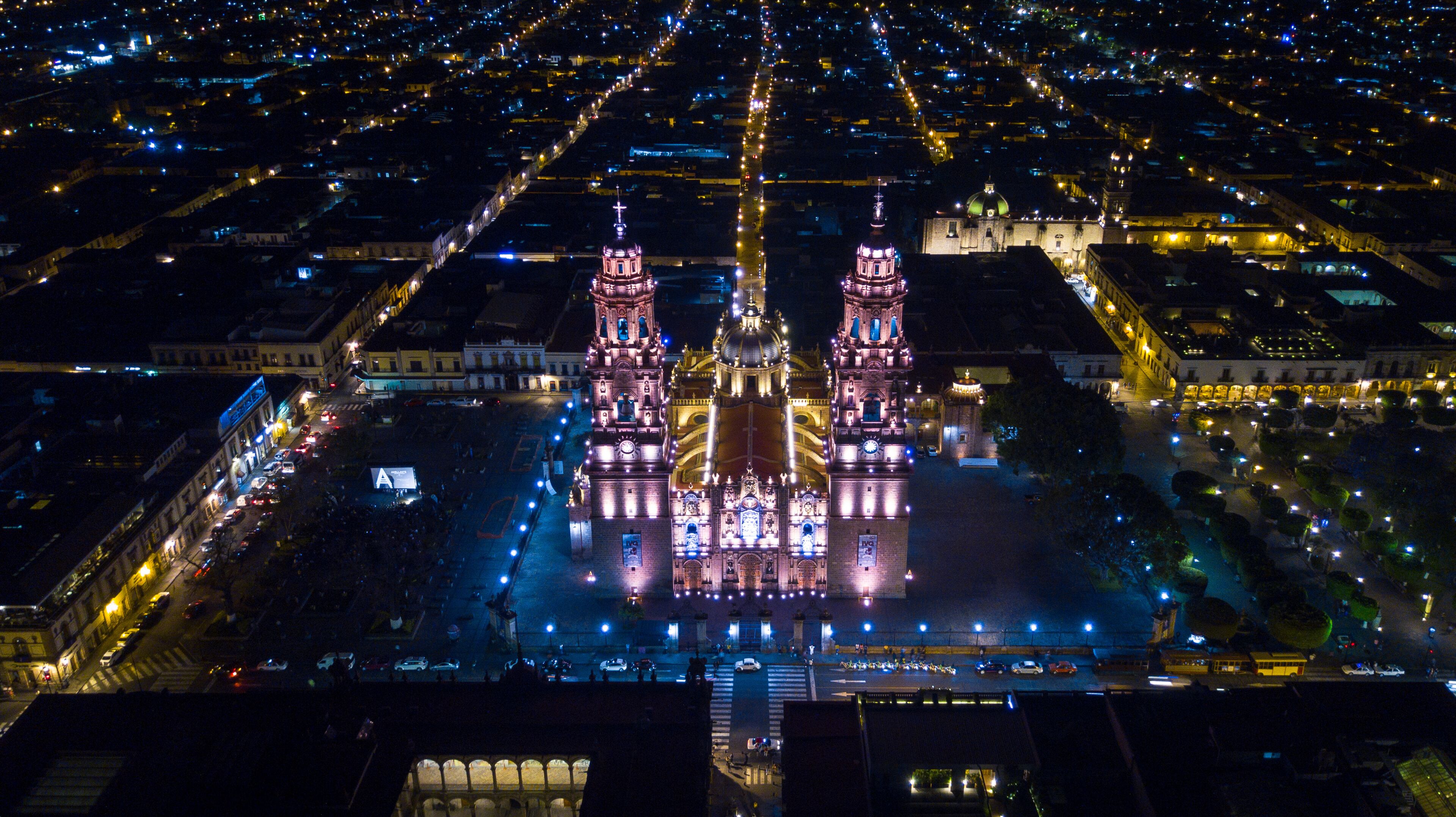 A brightly lit cathedral with two towers and a dome, surrounded by a cityscape at night.