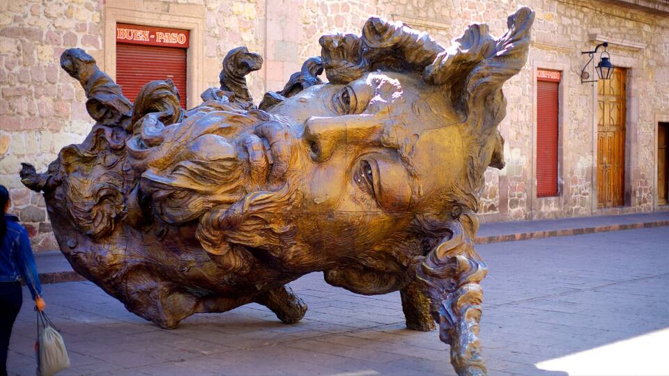 A large bronze sculpture of a bull in a dynamic pose, located in a public square with stone buildings in the background.
