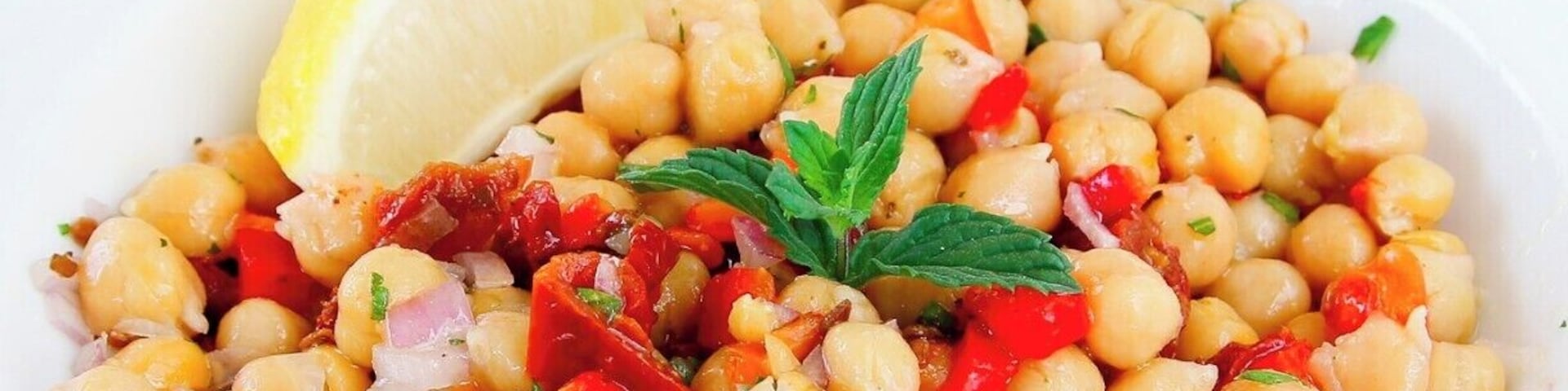 Un tazón de ensalada de garbanzos con adorno de limón y menta.
