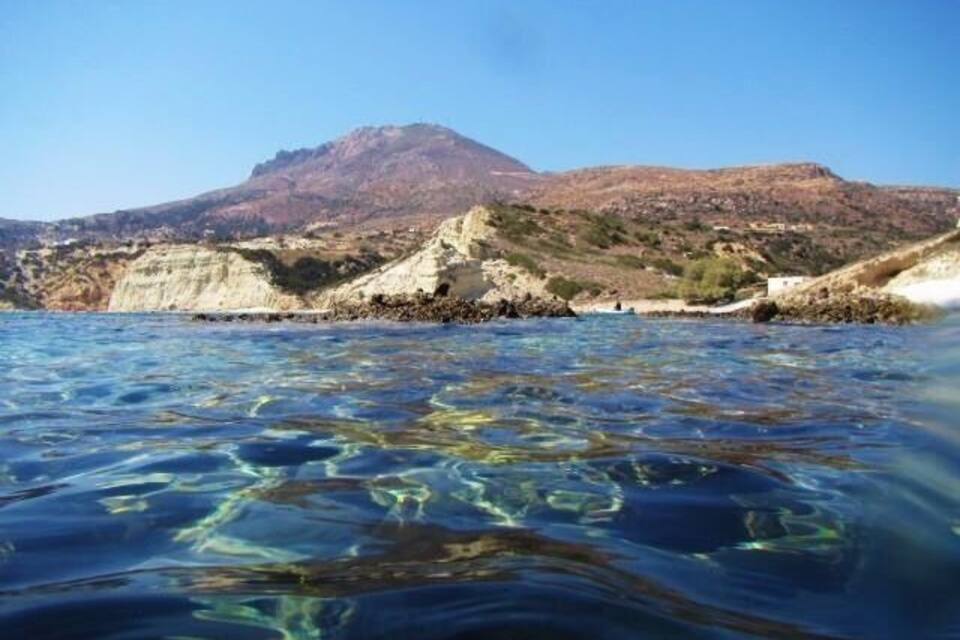 A coastal landscape with clear water, rocky cliffs, and a mountain in the background.