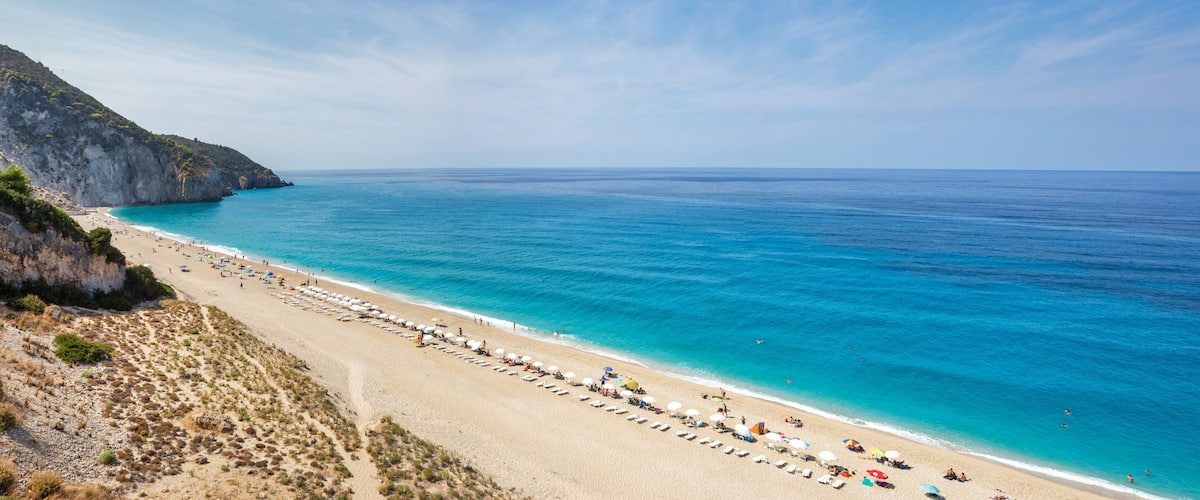 A coastal landscape with a sandy beach, a rocky cliff, and a clear blue sea.