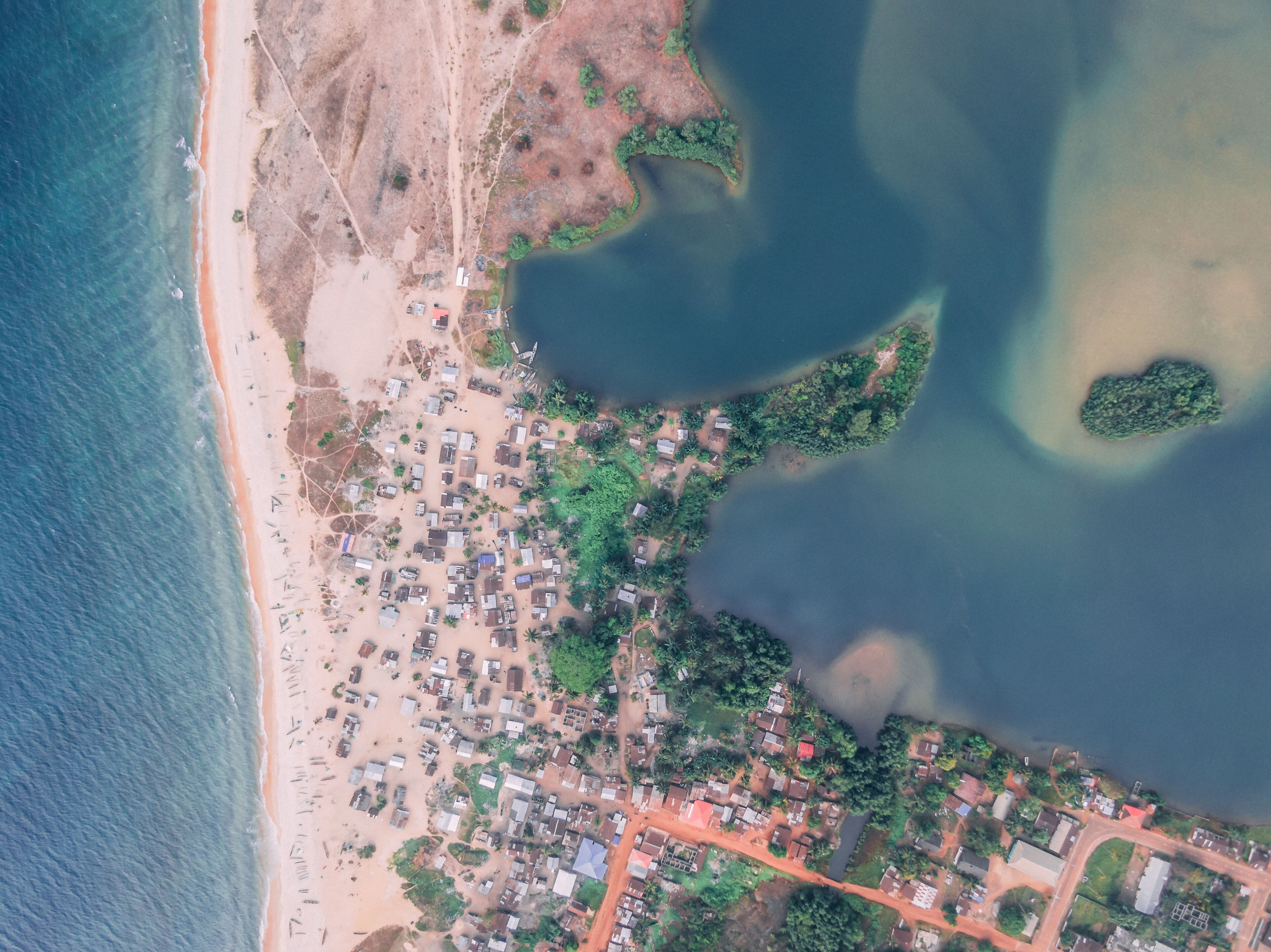 A coastal town with a beach, dense vegetation, and a large body of water.
