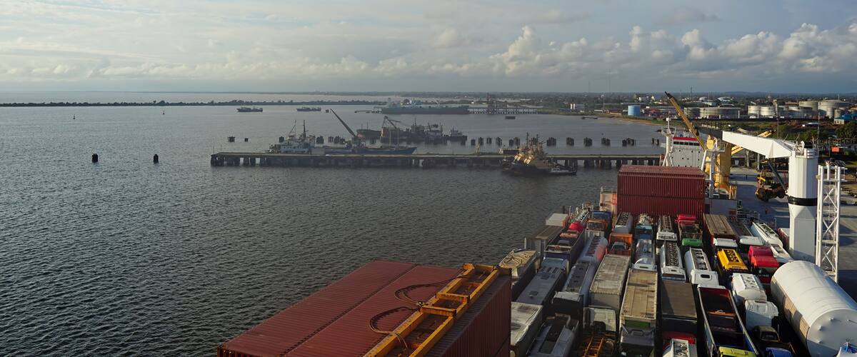 A busy port with cargo ships, cranes, and a large industrial area in the background.