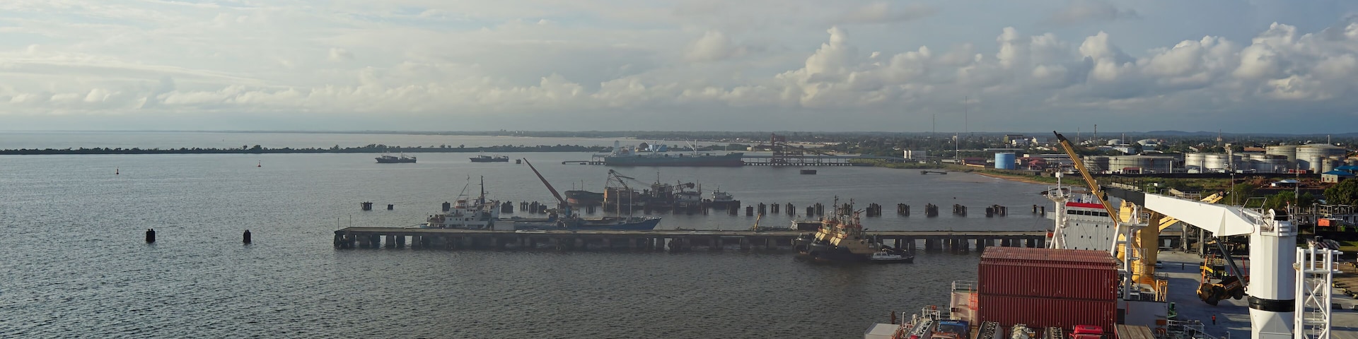 A busy port with cargo ships, cranes, and a large industrial area in the background.