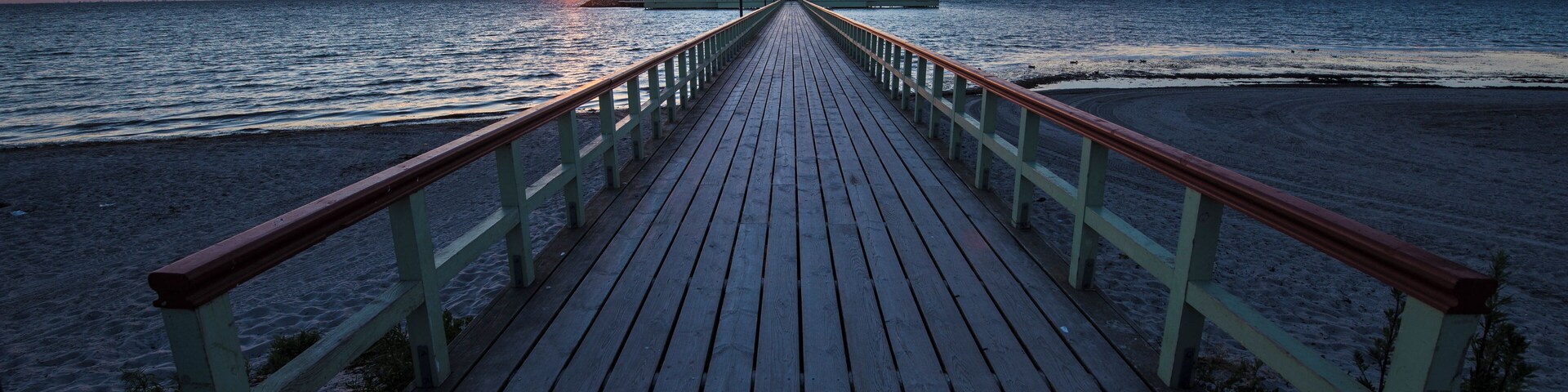 Un muelle de madera que conduce a la playa con un atardecer de fondo.