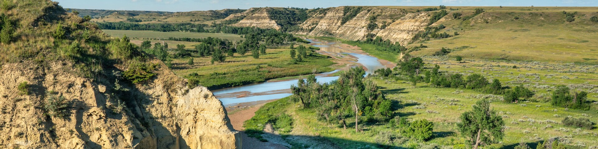Un río serpentea por un valle, con un risco a la izquierda y un paisaje cubierto de hierba y árboles.