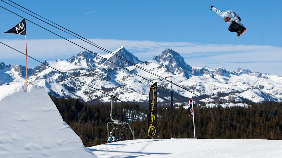A snowboarder mid-air with a snowy mountain backdrop, ski lift, and flags.