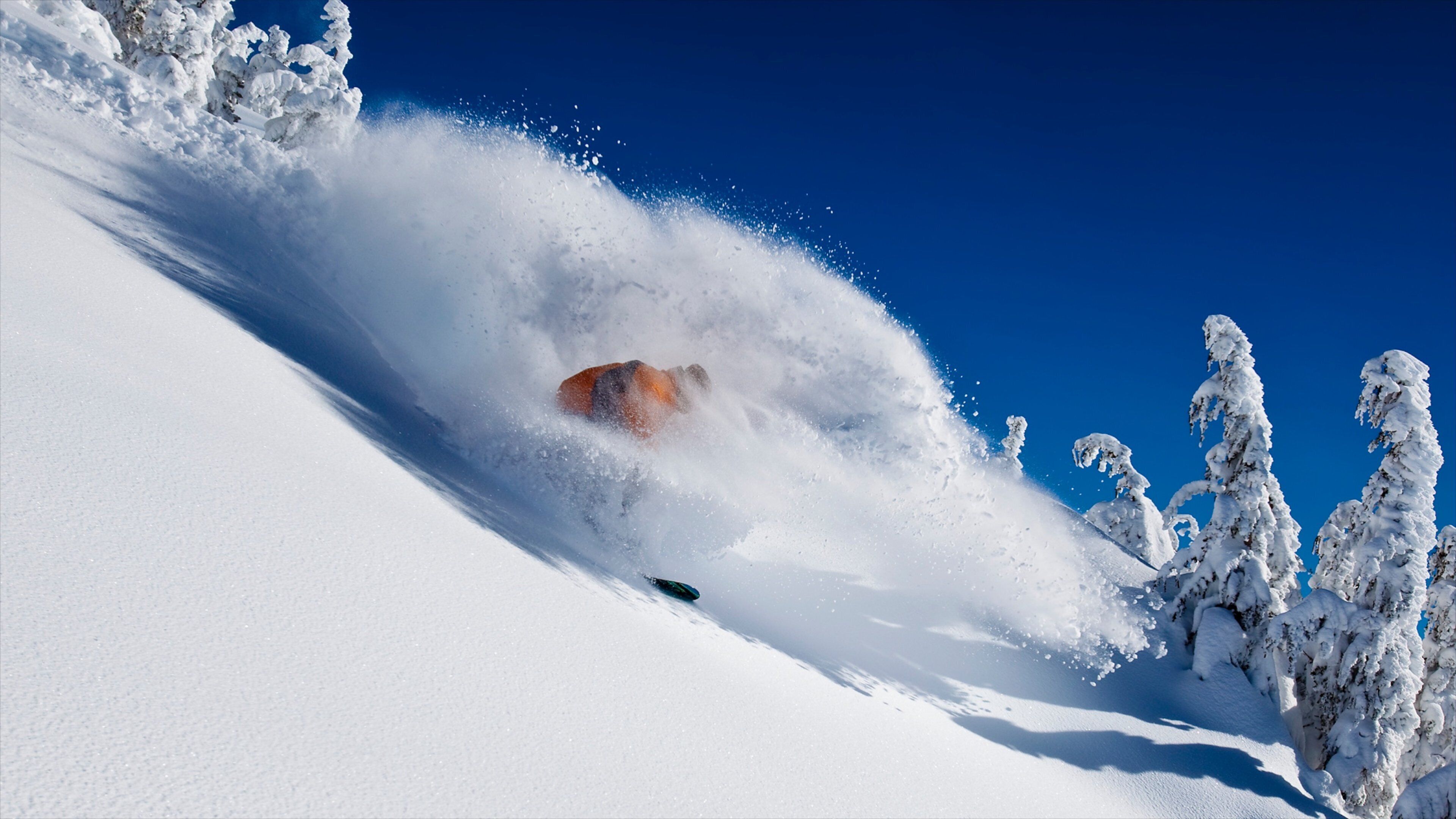 A snowboarder carving through deep snow with a clear blue sky in the background.