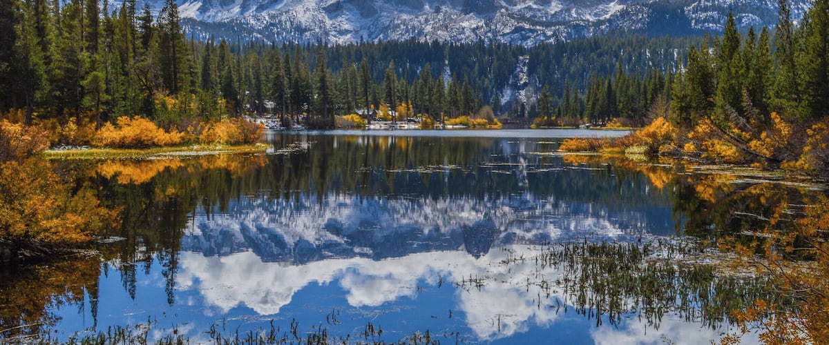 A mountain lake surrounded by autumn-colored trees and snow-capped mountains.