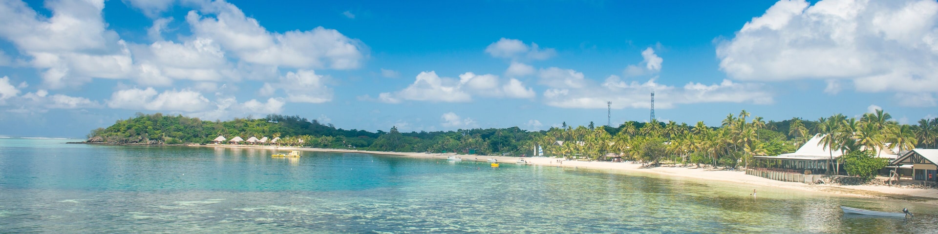 Una playa tropical con aguas turquesas cristalinas, una orilla de arena y una pequeña isla con vegetación y edificios.