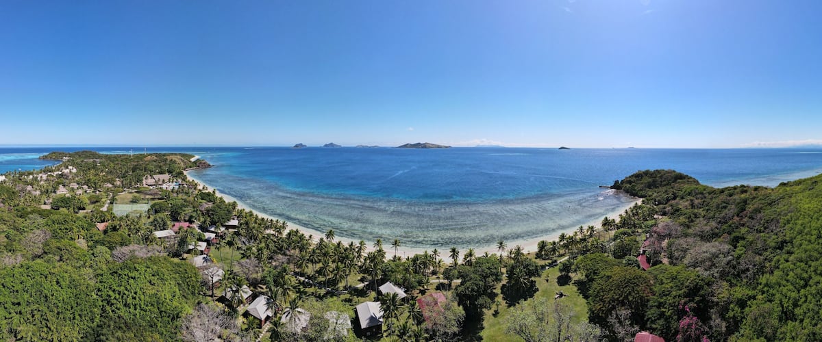 A coastal landscape with a beach, palm trees, and distant islands.