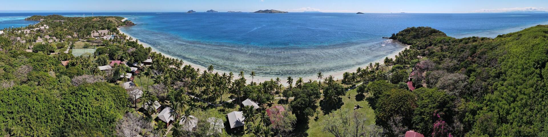 A coastal landscape with a beach, palm trees, and distant islands.