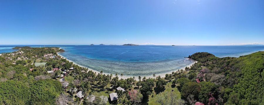 A coastal landscape with a beach, palm trees, and distant islands.