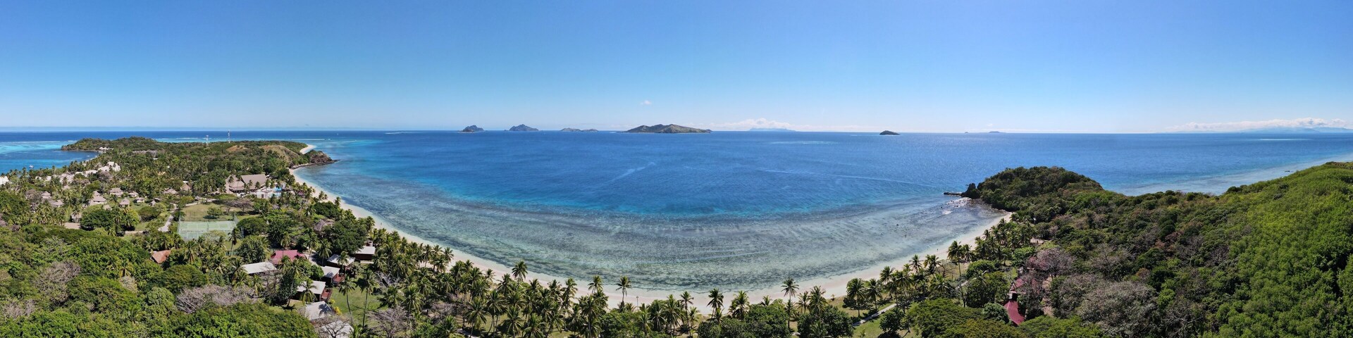 Un paisaje costero con una playa, palmeras y islas a lo lejos.
