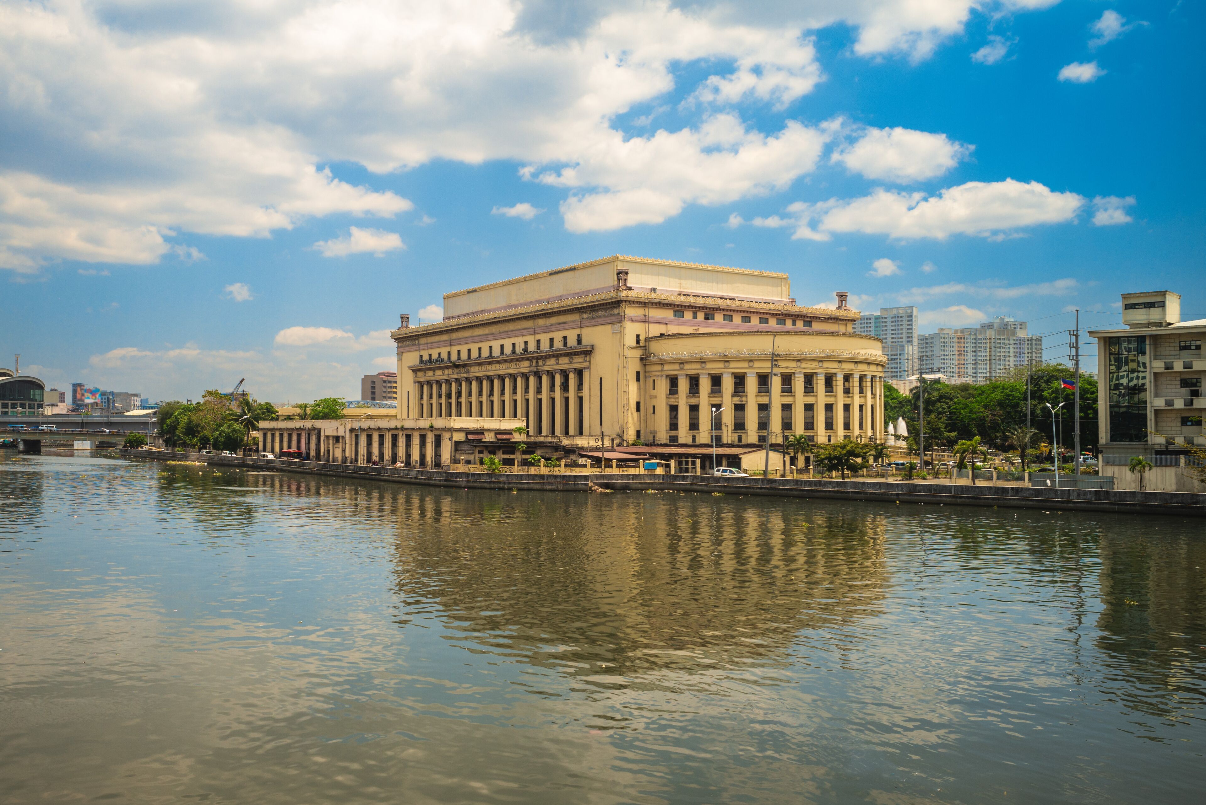 A large classical building by a river with a clear sky.